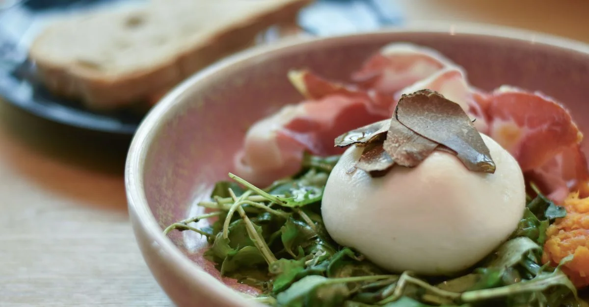 Une délicieuse salade de burrata gourmet avec de la roquette, du prosciutto et des copeaux de truffe, parfaite pour un brunch haut de gamme.