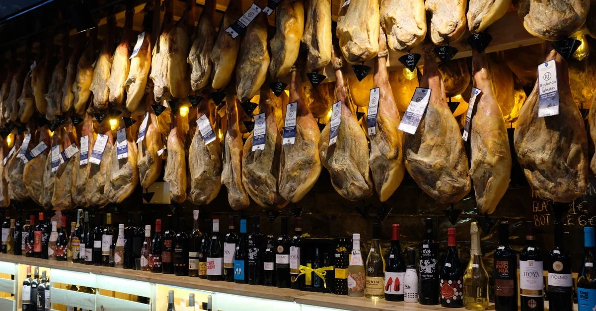 Une vitrine vibrante de jambon espagnol suspendu avec des bouteilles de vin dans un marché de Barcelone.