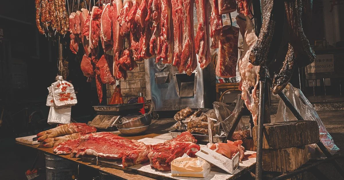 Une variété de viandes suspendues dans un comptoir de marché traditionnel sous un éclairage chaleureux, mettant en valeur une ambiance rustique.