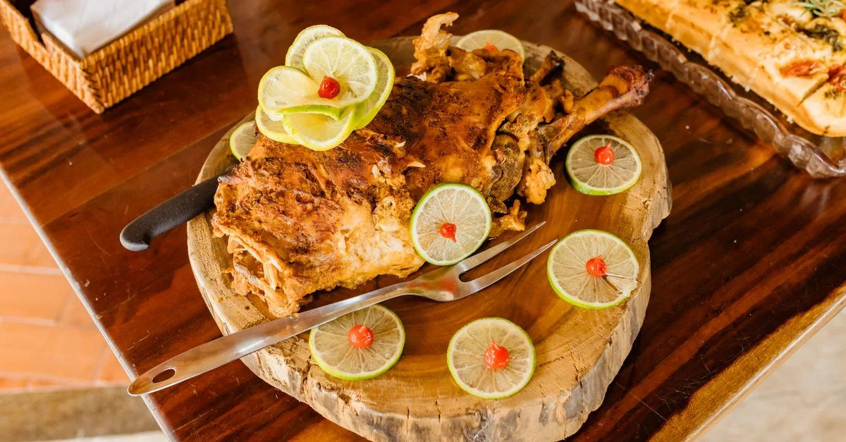 Délicieuse viande d'agneau rôti servie avec des tranches de citron vert et des garnitures sur un plateau en bois.