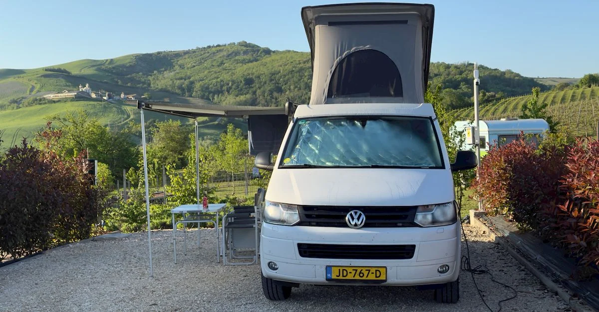 Un camping-car blanc garé dans un vignoble italien pittoresque sous un ciel bleu azur.