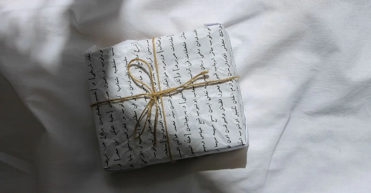 Cadeau magnifiquement emballé avec du papier cadeau en écriture arabe et un nœud en ficelle sur une surface blanche.