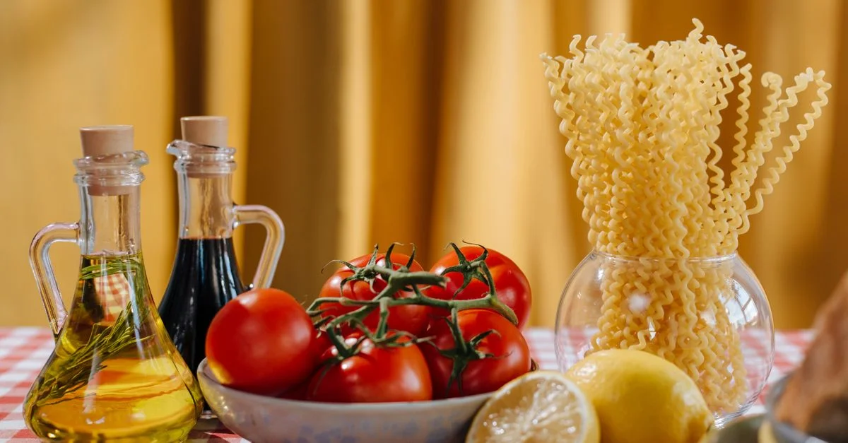 Nature morte vibrante d'ingrédients de cuisine italienne comprenant des tomates, des pâtes et de l'huile d'olive sur une nappe à carreaux.