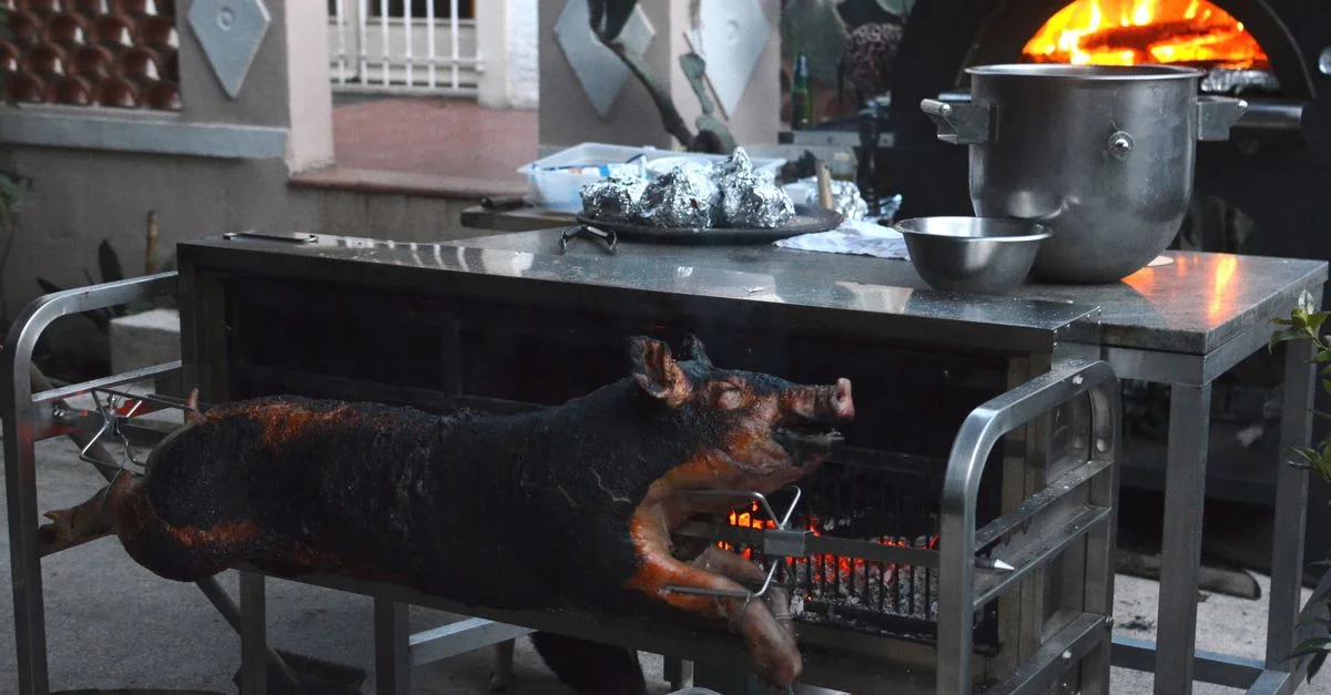 Rôtissage traditionnel de porc en extérieur avec un four, mettant en valeur des méthodes culinaires rustiques.