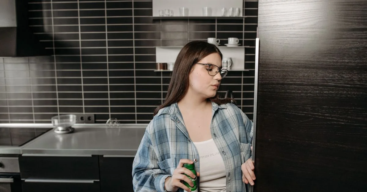 Une femme tenant une boisson ouvre le réfrigérateur dans une cuisine moderne et élégante.
