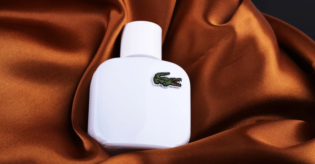 Bouteille de parfum blanche avec logo crocodile reposant sur une soie brune riche, présentant élégance et sophistication.