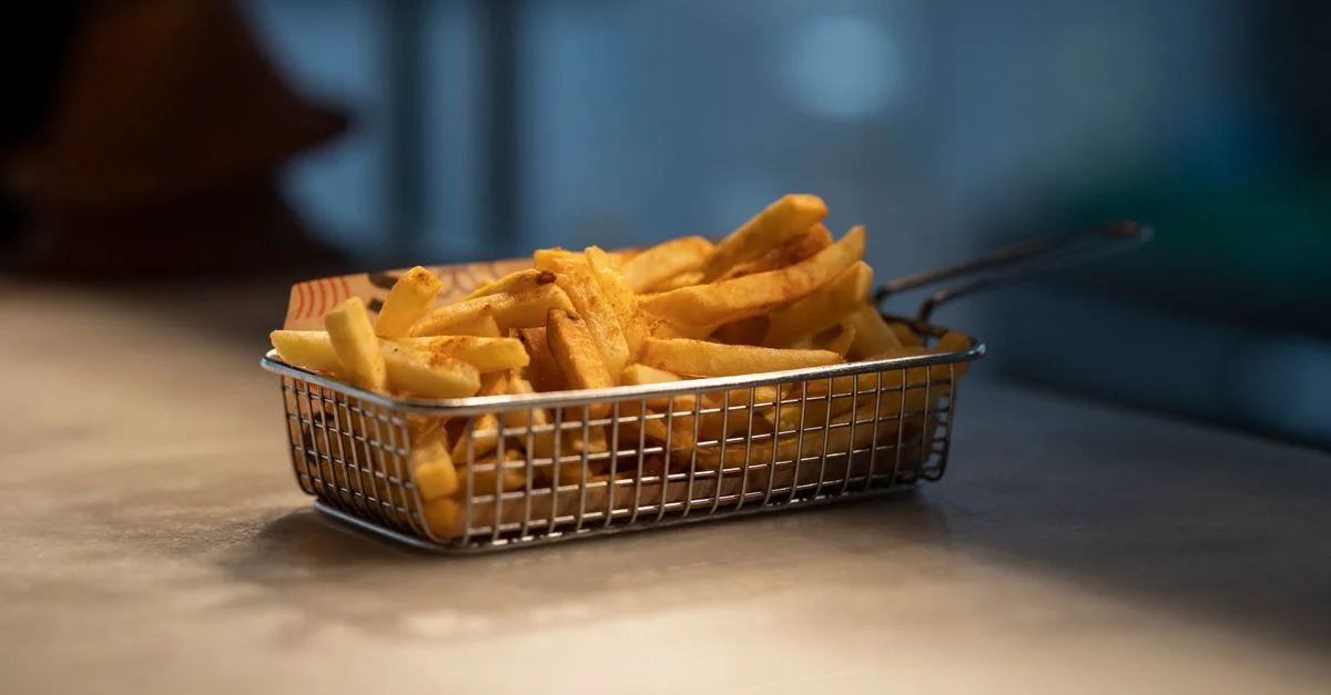 De délicieuses frites dorées servies dans un panier en acier sur une table. Parfait pour la photographie culinaire.