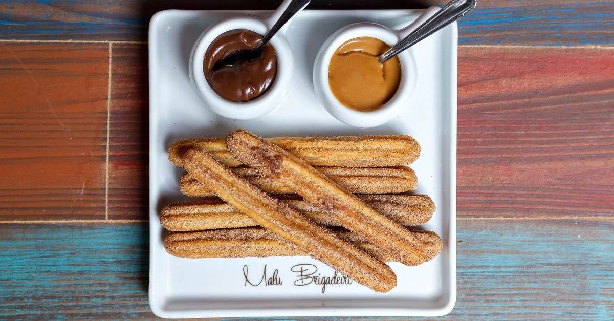 Assiette de churros avec des dips au chocolat et au caramel sur une table en bois colorée.