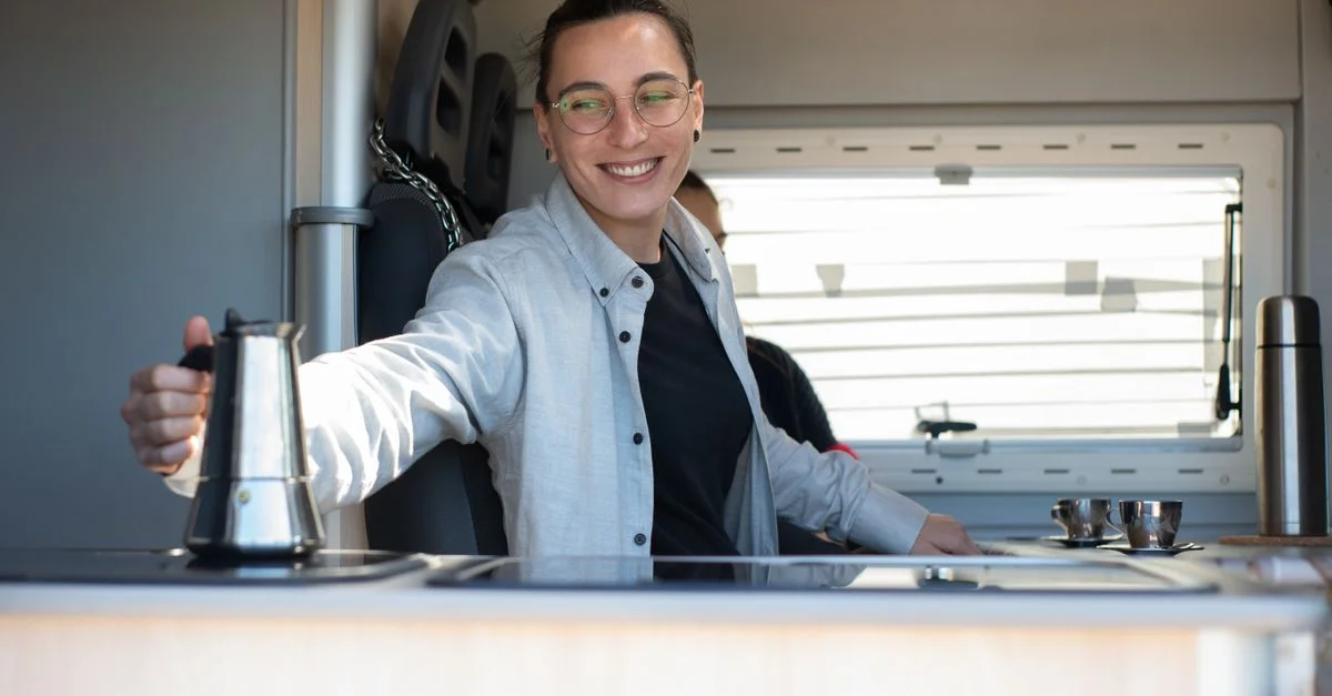 Une personne caucasienne souriante préparant du café dans une cuisine de camping-car au Portugal.