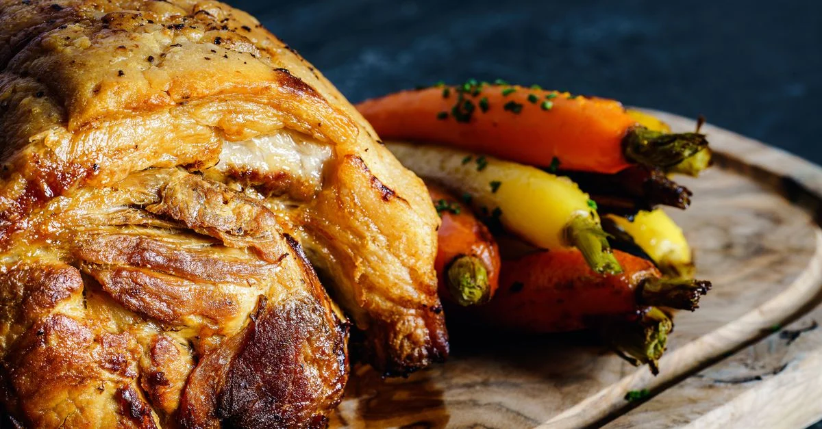Délicieux porc rôti servi avec des carottes colorées sur une planche en bois.