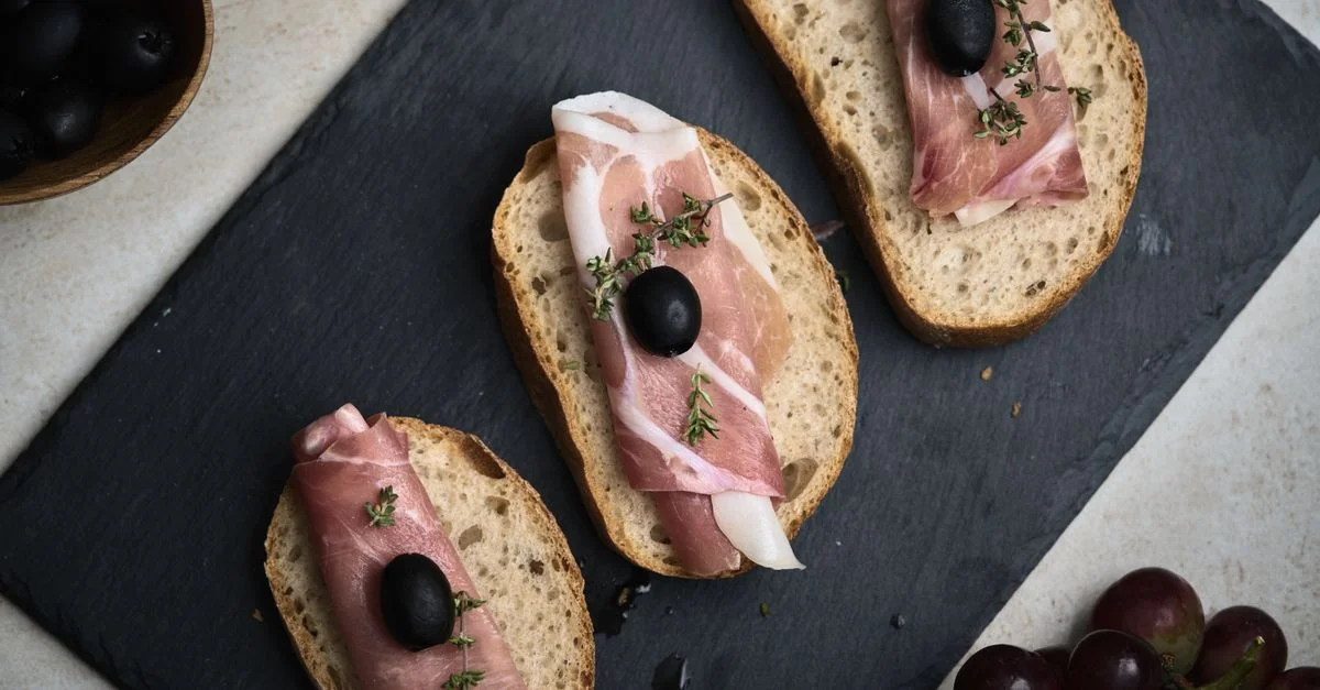 Vue aérienne de bruschetta méditerranéenne avec jambon et olives servie sur ardoise.