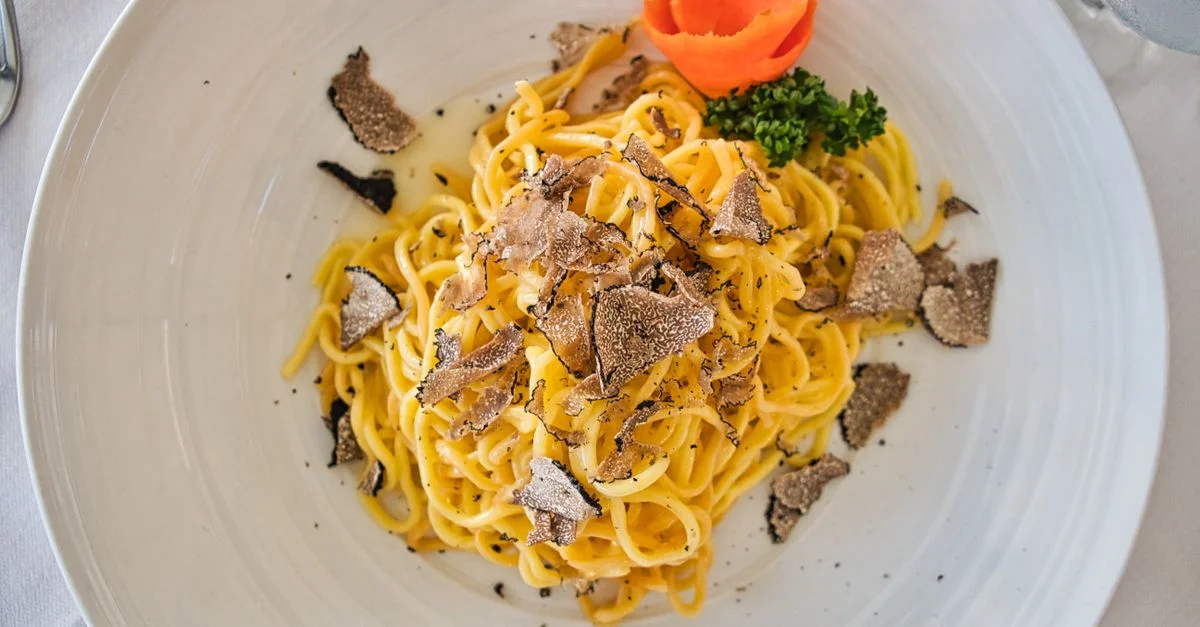 Délicieuse pâte gourmet servie avec des copeaux de truffe et une garniture colorée sur une assiette blanche.