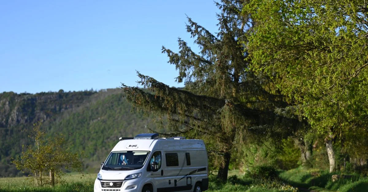 Un camping-car garé dans un paysage verdoyant et luxuriant avec un ciel clair, parfait pour les aventures en plein air.
