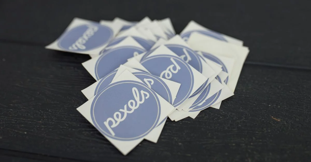 Une pile d'autocollants de logo Pexels disposés sur une surface en bois foncé.