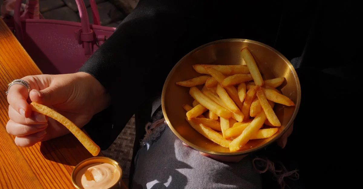 Main tenant des frites, un bol de frites, une sauce à tremper sur la table.